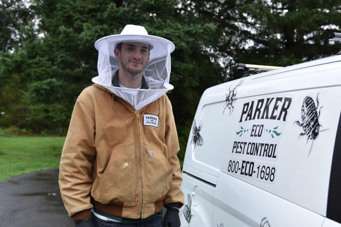 Pest control worker in beekeeping gear standing next to a van