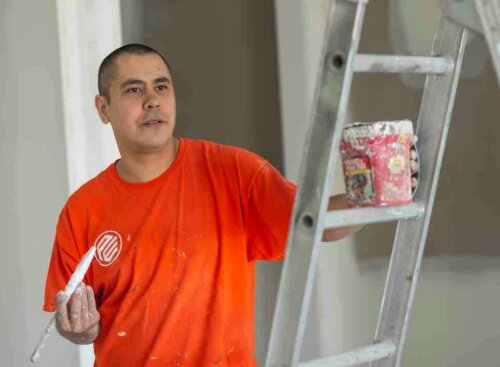 painter holding brush and paint can near ladder